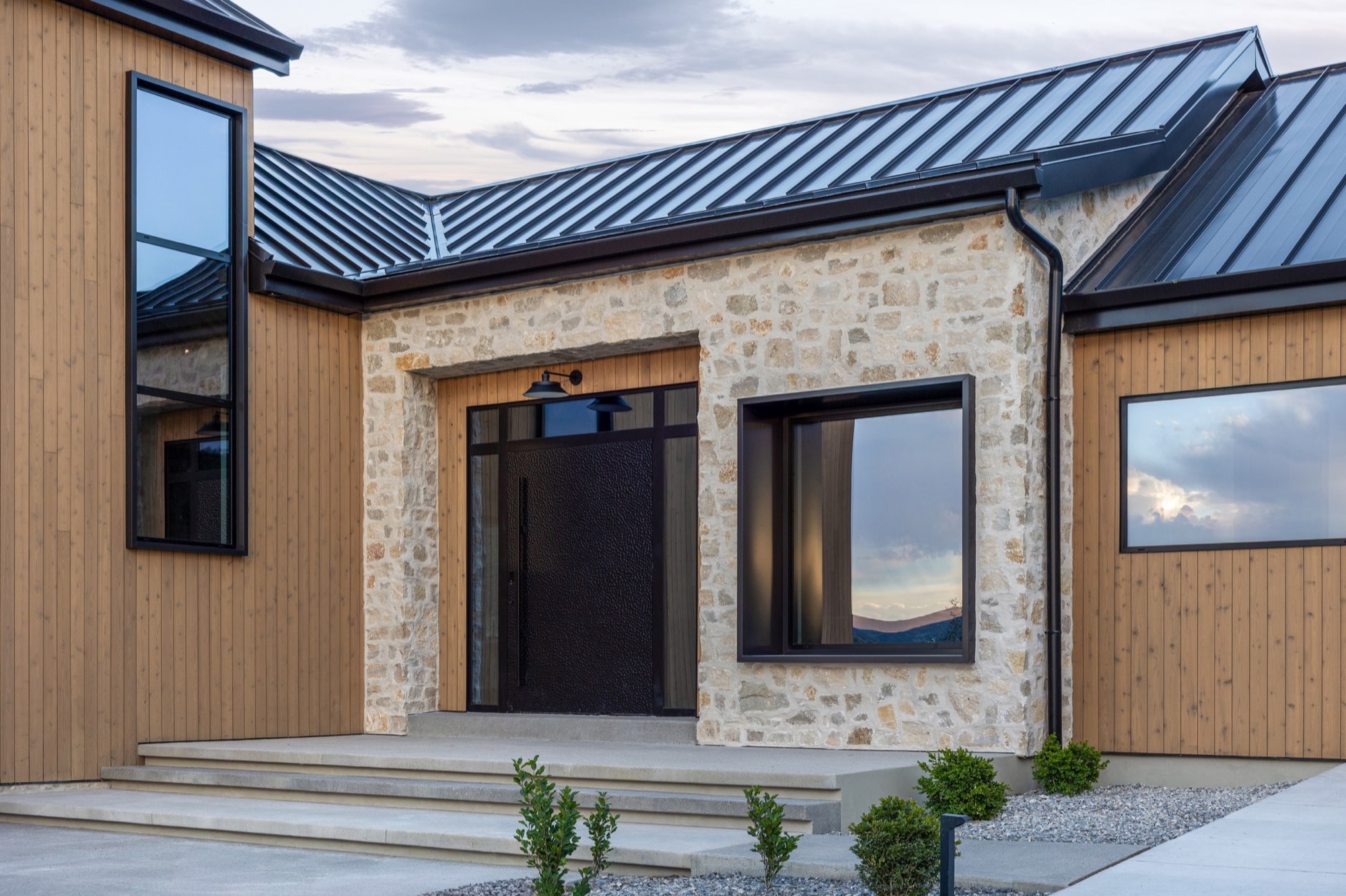 Lumen — entry portal with stone surround and black textured door at dusk