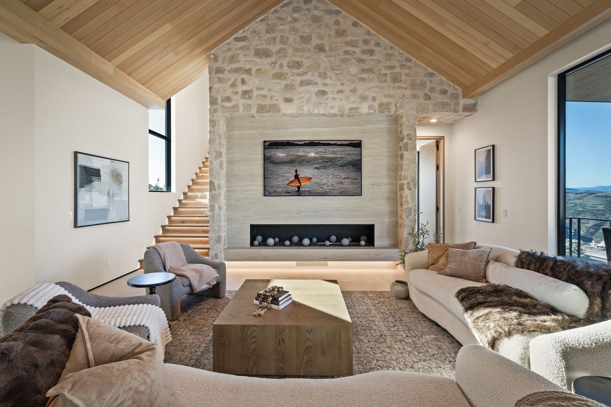 Lumen — great room under a vaulted cedar ceiling with a full-height stone fireplace and floating stair