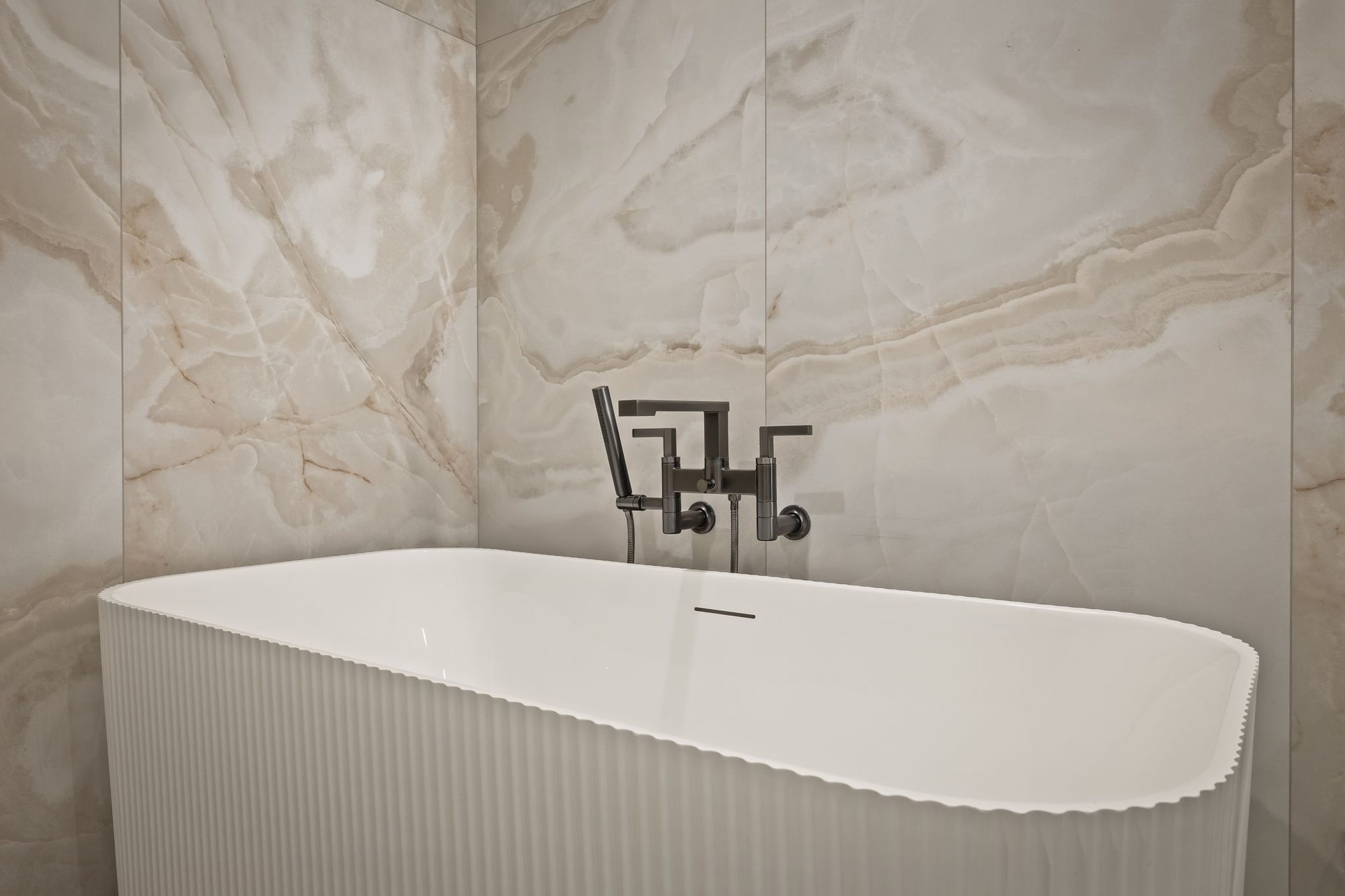 Lumen — freestanding tub against book-matched stone in the primary bath