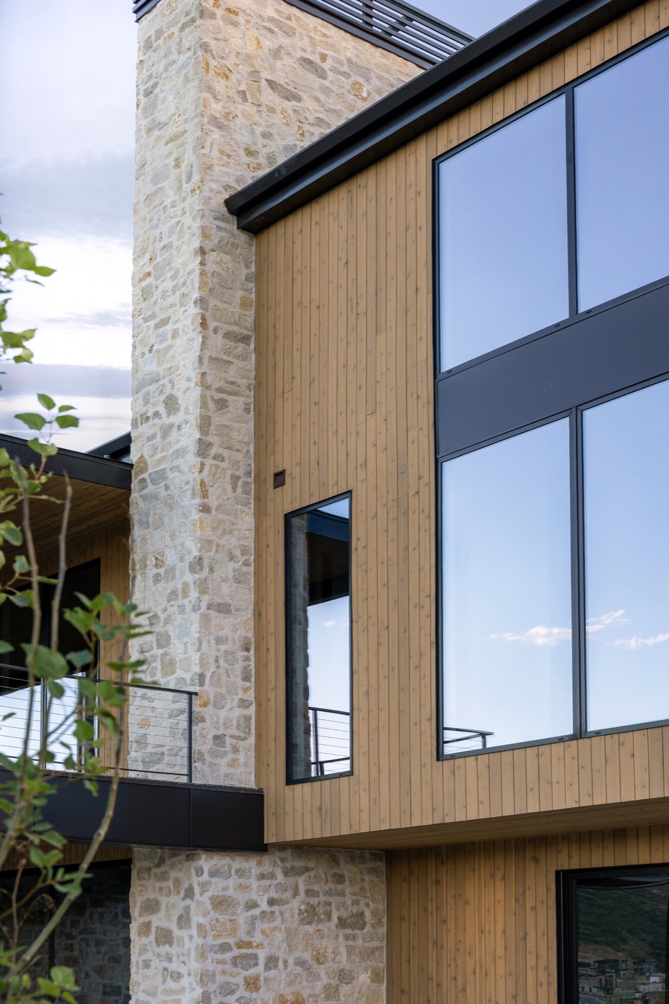 Lumen — stone chimney and glass corner detail with cable-rail balcony